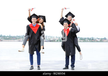 Gerne Studenten in Bachelor- Roben und mit den Diplomen im Freien Stockfoto