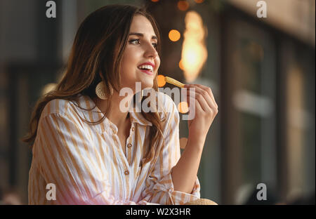 Schöne junge Frau essen lecker Pommes Frites im Freien Stockfoto