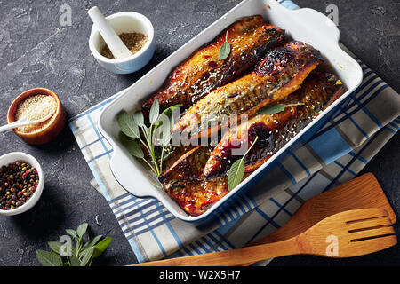 Lecker gebratene Filets von Makrele Fisch in einer Auflaufform auf einer konkreten Tabelle mit Gewürzen im Hintergrund, Ansicht von oben Stockfoto