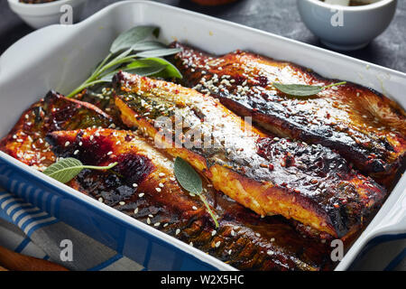 Close-up lecker gebratene Filets von Makrele Fisch in einer Auflaufform auf einen konkreten Tisch mit Gewürzen im Hintergrund, Ansicht von oben, Ma Stockfoto