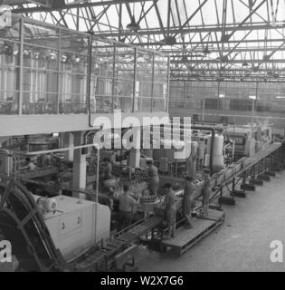 1950er Jahre, historische Erwachsene Männer und Frauen in Overalls, die in der Produktionshalle einer großen Abfüllanlage des Getränkeherstellers Farsons in Malta arbeiten. Stockfoto