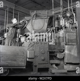 1950 s, historischen, einen männlichen Arbeitnehmer in Overalls mit Maschinen am stets bereit, Batterie Fabrik in Walthamstow, London, England, UK. Die Fabrik produziert Zink-Kohle-Batterien, die waren die ersten kommerziellen chemische Batterien. Stockfoto
