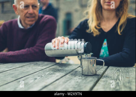 Eine junge Frau und ein älterer Mann gießen Wasser aus einer Flasche an einem Tisch draußen Stockfoto