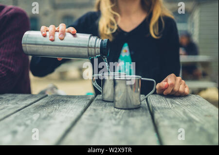 Eine junge Frau ist das Gießen von Wasser aus einer Flasche im Freien an einem Tisch Stockfoto