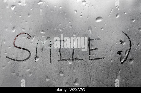 Handgefertigte Wort Lächeln auf dem nassen Glas Fenster Stockfoto