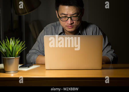 Asian Business Mann nachts arbeiten, freiberuflicher Programmierer oder Entwickler arbeiten zu Hause auf, und geben Sie den Quellcode mit Laptop, Ernst und Überstunden anhand von quantitativen Simulatio Stockfoto
