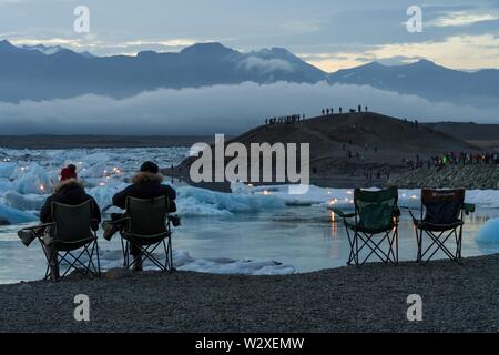 Touristen im Camping Stühle für Feuerwerk auf der Gletscherlagune Jokulsarlon, Massentourismus, South Island, Island warten Stockfoto