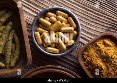 Curcuma Kapseln, Kurkuma Wurzeln und Pulver in Schalen. Anti Krebs Medizin. Holztisch. Ansicht von oben geschossen. Stockfoto