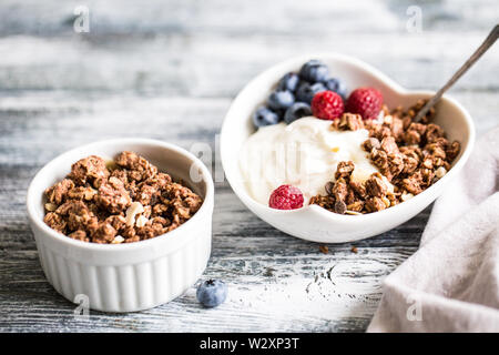 Griechischer Joghurt, Blaubeeren, Himbeeren und Müsli in einer weißen Schüssel auf einem hölzernen Hintergrund. Stockfoto