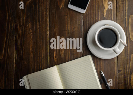 Schwarzen Kaffee, Stift und Notebook auf dunklen Holztisch. Arbeitsplatz Stockfoto