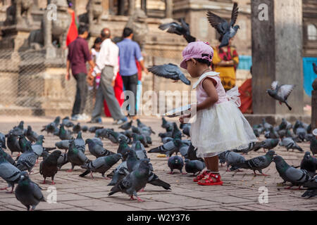 Junge Mädchen mit einem hübschen Kleid füttern Tauben in einem Tempel in Kathmandu Stockfoto