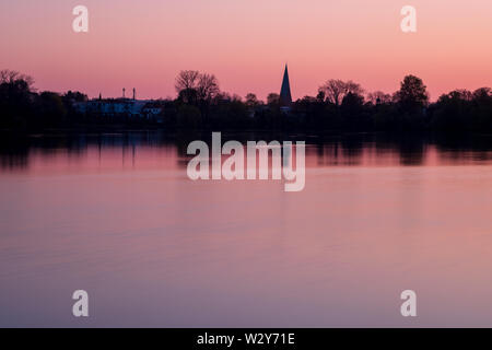 Rot und rosa Sonnenuntergang über ruhige See mit Silhouette der Stadt Eutin mit churchtower, Schleswig-Holstein Stockfoto