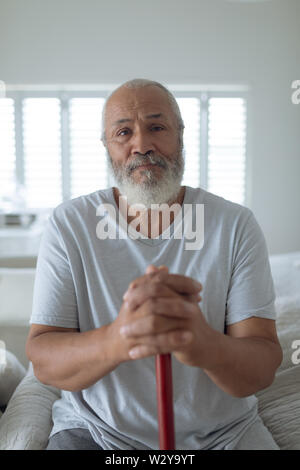 Mann sitzt auf dem Bett, während Sie eine hölzerne Spazierstock Stockfoto