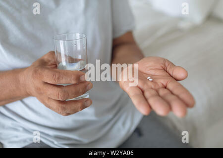 Mann sitzt auf dem Bett, während sie Pillen und ein Glas Wasser Stockfoto