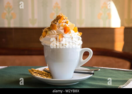 Kaffee mit Sahne und getrockneten Früchten in Weiß der Tschechischen auf einem Tisch in einem Cafe mit einem kleinen Cookie auf eine Untertasse, Löffel und Stroh. Köstliches Dessert in t Stockfoto
