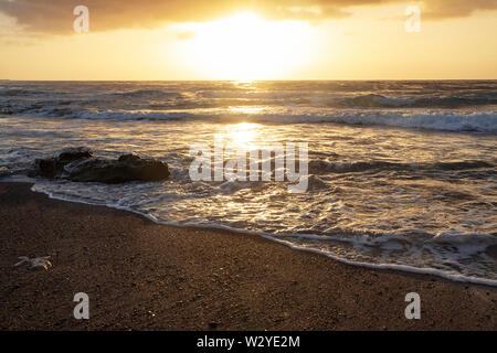 Dramatischer Sonnenaufgang mit Wellen, die über den felsigen Strand in El Medano, Teneriffa, Kanarische Inseln, Spanien Stockfoto