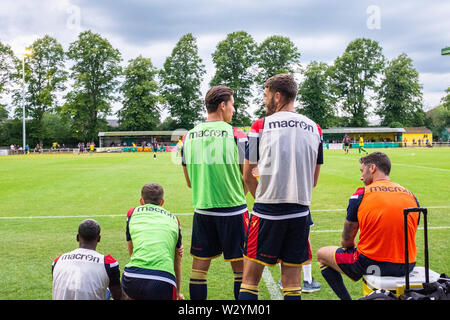 Ersatz-Spielern Chatten und Aufwärmen auf der Seitenlinie während des Spiels an der unteren Liga, non League Ground Stockfoto