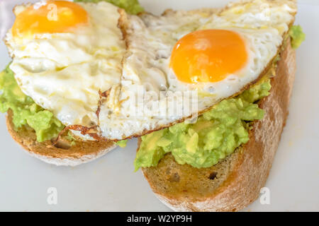 Zwei Spiegeleier auf Guacamole auf dicken Vollkorn toast Stockfoto