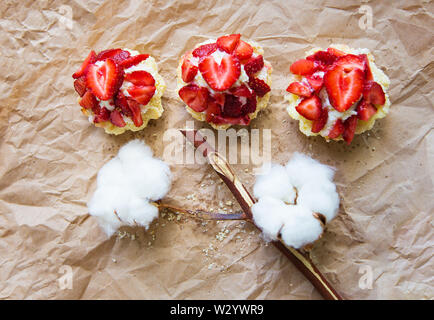 Schöne kleine Kuchen mit Erdbeeren zusammen mit einem Zweig der Baumwolle liegt auf Kraftpapier. Stockfoto