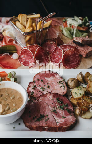 Traditionelle Luxemburger Gericht Judd mat Gaardebounen, geräucherte Kragen Schweinefilet mit Bohnen, auf einem Schild neben kalte Fleischplatte, selektive konzentrieren. Stockfoto