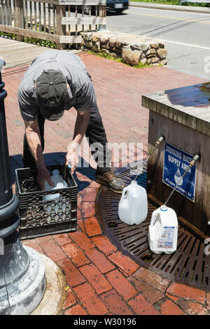 Sandwich, MA - 15. Juni 2019: Dieser Mann ist Wasser beim Füllen Krüge aus der öffentlichen Versorgung der freien Feder Wasser durch die alte Schrotmühle. Stockfoto