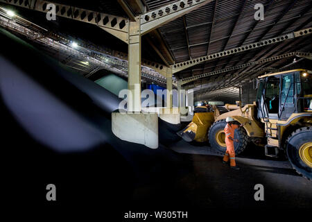 Bergbau, Verwaltung und Transport von Titanmineralsanden. Im Inneren des Ilmenit- und Rutil-Lagerhauses. Transport von Ilmenit vom Bunker zum Lastförderer. Stockfoto