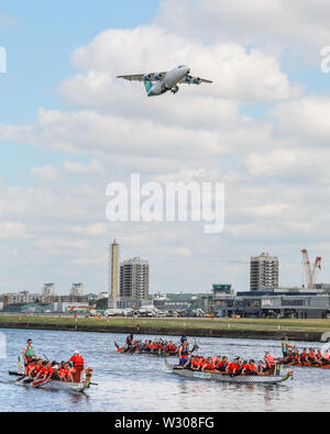 Ein Flugzeug hebt ab London City Airport als Rennfahrer in ihren Drachen Boote auf dem Wasser zu London Hong Kong Dragon Boat Festival an der Königlichen konkurrieren Stockfoto