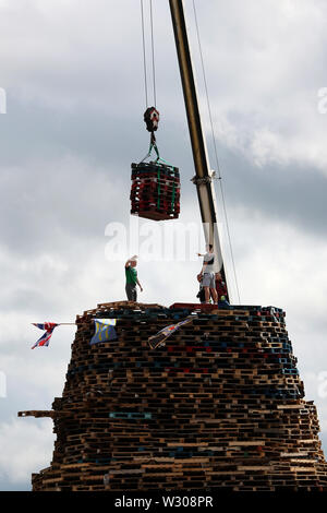 Bonfire Erbauer in der Sandy Row Bereich von Belfast als Gebäude weiterhin auf die loyalistischen Lagerfeuer, die sich traditionell auf die elfte Nacht beleuchtet werden, die in der Zwölften Gedenkfeiern zu etablieren. Stockfoto