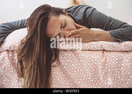 Das Mädchen liegt im Bett und gähnt. Sie umfasst den Mund mit der Hand. Am frühen Morgen und Sie ist müde. Stockfoto