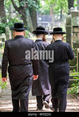 Jüdische Chasidic Männer in traditionellen lange schwarze Mäntel und Hüte sprechen Sie ein Gebet an einem alten Grabstein in der Neuen Jüdischen Friedhof in Kazimierz in Krakau, Polen Stockfoto