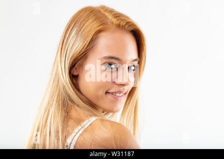 Charismatische junge Frau mit einer warmen, freundlichen Lächeln in die Kamera über die Schulter zu schauen, in der Nähe portrait isoliert auf weißem Stockfoto