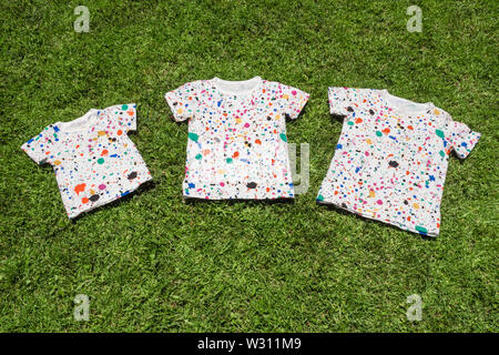 Drei T-Shirts liegen auf grünem Gras. Sommerlager für Kinder, konzeptionelle. Große familie Hintergrund. Behandlung der Geschwister. Prozess der Lehre Stockfoto