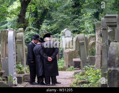 Jüdische Chasidic Männer in traditionellen lange schwarze Mäntel und Hüte sprechen Sie ein Gebet an einem alten Grabstein in der Neuen Jüdischen Friedhof in Kazimierz in Krakau, Polen Stockfoto