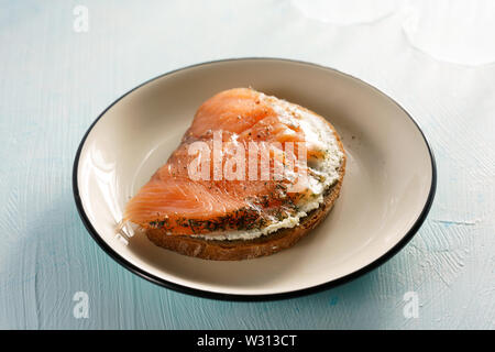 Roggen Toast mit Frischkäse, Lachs und Pfeffer. Weißer Keramik Teller, blau Tisch, hohe Auflösung Stockfoto