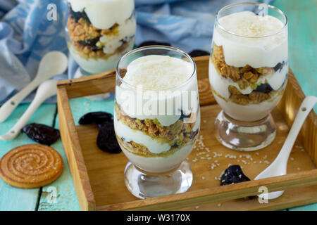 Veganes Dessert mit Schlagsahne, Nüssen, Haferflocken, Pflaumen und Sesam in Glas Gläser auf einer hölzernen rustikalen Tisch. Stockfoto