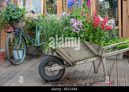 Alte Schubkarre und Fahrrad vor ein Gewächshaus auf einem Display an der RHS Hampton Court Flower Show 2019. Hampton Court, Surrey, England Stockfoto