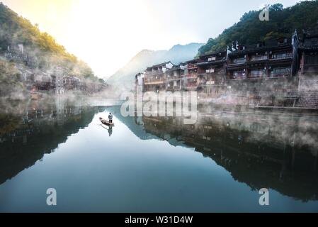 Ein lokaler Mann Reinigung der Fluss wie die Sonne in Fenghuang, China steigt. Stockfoto