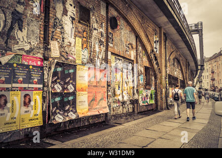Berlin, Deutschland - 15. Juni 2019: Zerkratzt bunten Werbeplakaten entlang der Bahnhof Berlin Alexanderplatz. Menschen gehen für einen Spaziergang entlang der Stockfoto