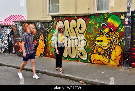 Zwei Menschen zu Fuß entlang der Straße in St Paul's Bristol mit Street Art hinter während der Karnevalszeit Stockfoto