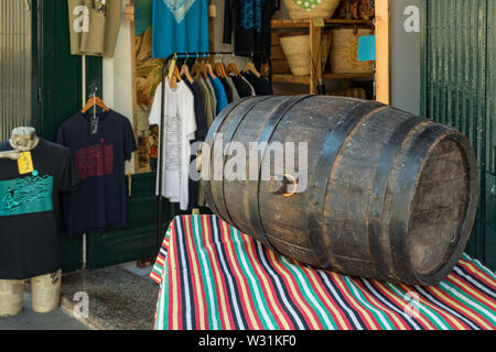 Puerto de la Cruz, Tenera, Spanien - 10. Juli 2019: Ein altes Weinfass liegt auf einem Tisch mit einer Tischdecke typischer kanarischer Volksfarben. T-sh Stockfoto