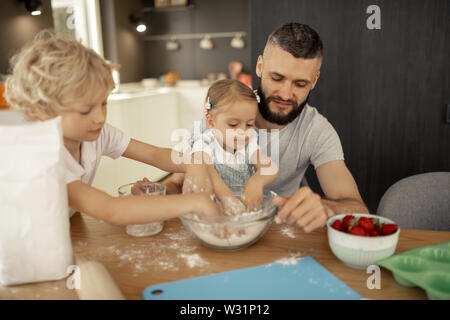 Hilfreich Kinder. Nette süße kleine Kinder die Hände in das Mehl, während ihr Vater helfen mit Kochen Stockfoto