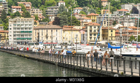 COMO, ITALIEN - JUNI 2019: Menschen zu Fuß auf dem Gehweg, die reicht bis in den Hafen in Como am Comer See. Stockfoto