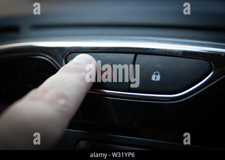 Ein Finger drücken der Taste der Warnblinkanlage auf einem Auto Innenraum Stockfoto