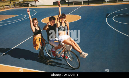 Gruppe von drei Freunden mit Skateboard und Fahrrad auf Basketball im Freien. Freunde heraus hängen im Freien. Stockfoto