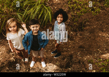 Drei Kinder zusammen in den Wald und Suchen an der Kamera. Multi-ethnischen spielende Kinder im Wald. Stockfoto