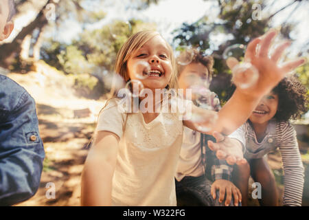 Gruppe von Kindern beim Spielen mit Seifenblasen im Wald. Mädchen mit Freunden fangen die Seifenblasen. Stockfoto