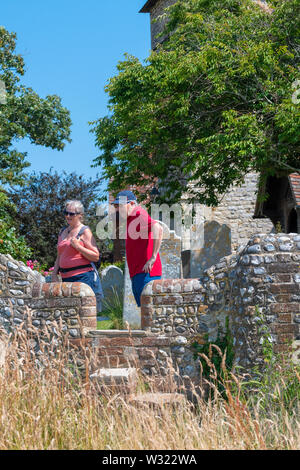 Spaziergänger auf einem öffentlichen Fußweg mit der Steintreppe Stile überqueren auf der Steinmauer in St. Peter und St. Paul Kirche, West Wittering, Großbritannien Stockfoto