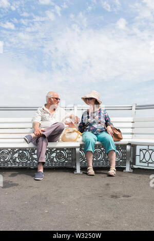 Eine ältere oder rentnerehepaar entspannten sitzen auf einer Bank an einem Sommertag sprechen Stockfoto