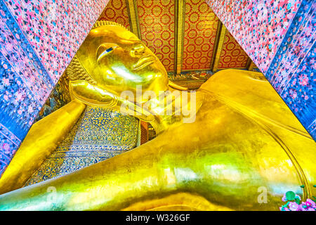 BANGKOK, THAILAND - 22 April, 2019: Die große goldene Skulptur des Liegenden Buddha liegt auf der Fliesen- Kissen in wunderschön gestalteten Viharn Phranorn t Stockfoto