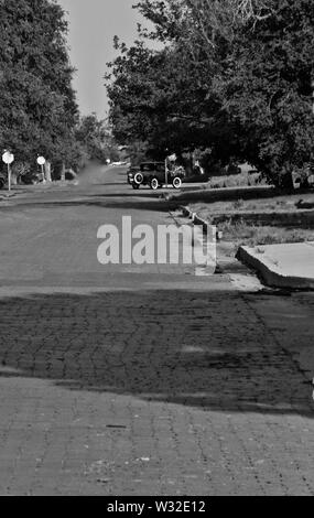 Altes Auto und Brick Road in Schwarz und Weiß gibt eine irgendwo in der Zeit Wirkung im Canyon, Texas. Stockfoto